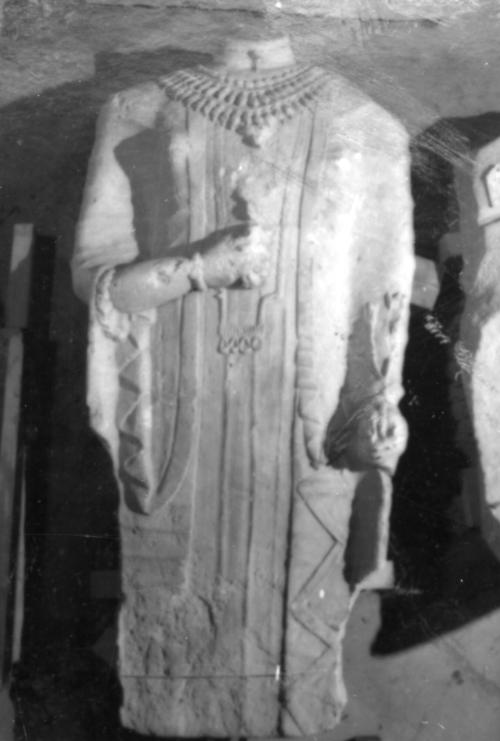 Female statue holding flowers and wearing a tunic, cloak, beaded choker with pendant, three-tiered pectoral necklace, long pendant with four seal-rings, and wrist bracelets