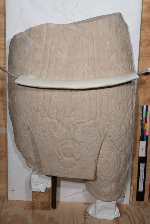 Lower torso and upper legs of a colossal male statue wearing a kilt with a head of Hathor flanked by uraeus snakes on the sash