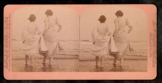 [Two women dipping feet in water at beach]