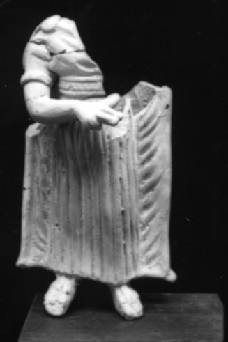 Female figurine in the pose of a lyre player wearing a belted short-sleeved tunic, cloak, sandals, and arm bracelet