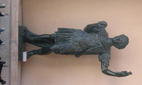 Figure is dressed as a warrior with orb in right hand and cylinder-shaped object in left hand