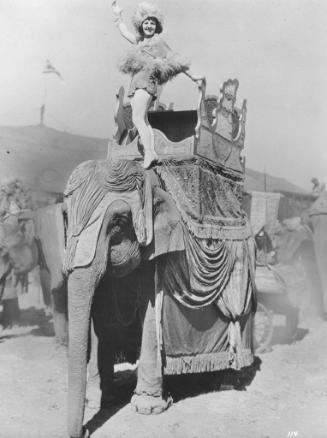 Zefta Loyal of the Repenski Troupe stands on an elephant's shoulder in a spec number.