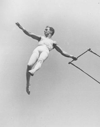 Alfredo Cordona swinging from a trapeze with his left hand on the trapeze bar.  1930.