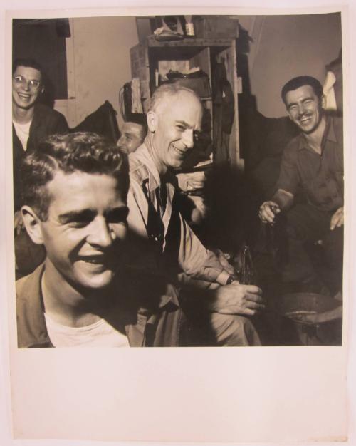 Young Man Smiles as Ernie Taylor Pyle Sits Enjoying a Coca Cola in the Middle Ground