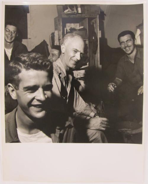 Young Man Smiles as Ernie Taylor Pyle Sits Enjoying a Coca Cola in the Middle Ground