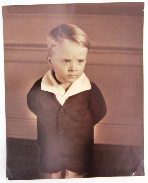 Blond Boy Stands with Arms Crossed Behind His Back in a Suit