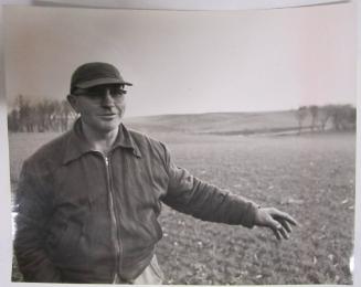 Man in Cap and Glasses in Field Gestures to the Left