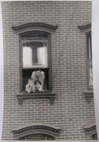 Woman and Two Children Lean out a Window of a Brick Building