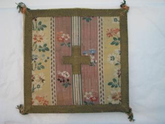 Square piece of fabric fringed on corners, a cross in the center and multiple rows of flowers o…